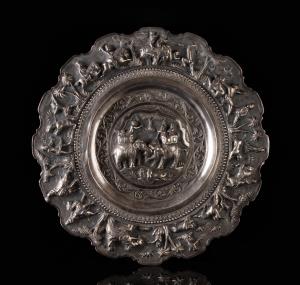 Of shallow circular form with crenellated rim, the repousse decoration in high relief, com